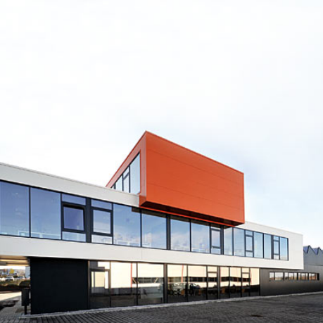 modernes dreistöckiges Gebäude mit großen Glasfronten, dritter Stock als kastenförmiger, orangefarbener Aufbau